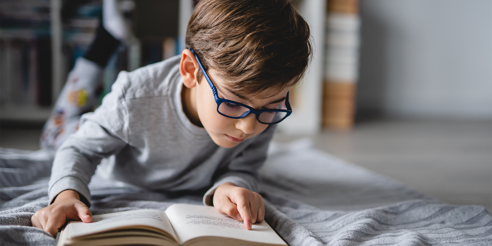 Elementary age boy reads a book while laying on the floor