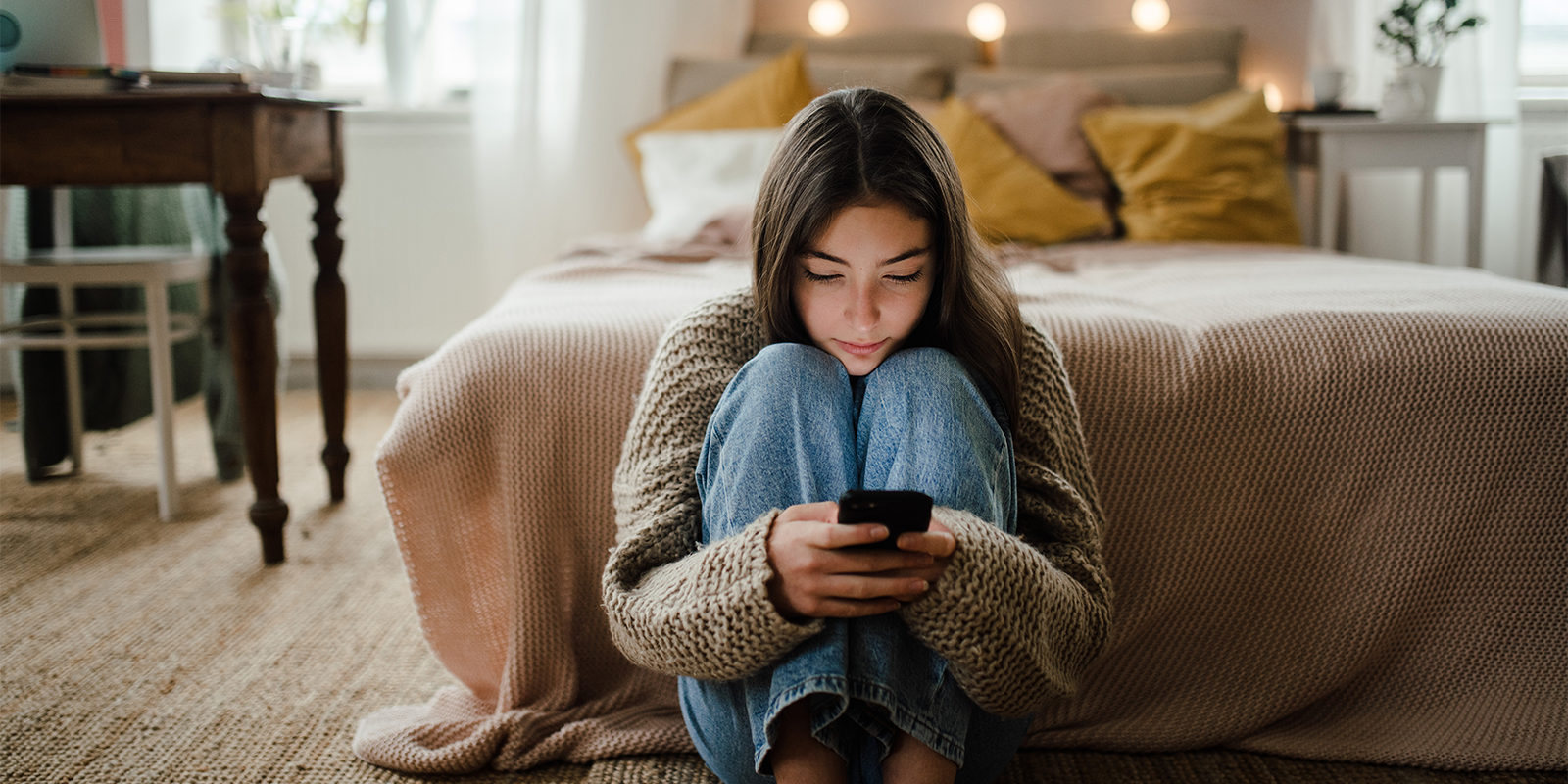 Teen girl looks at her cell phone while sitting in her bedroom