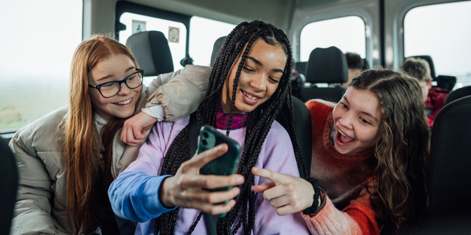 A diverse group of three girls smiling while looking at a smartphone in a close setting.