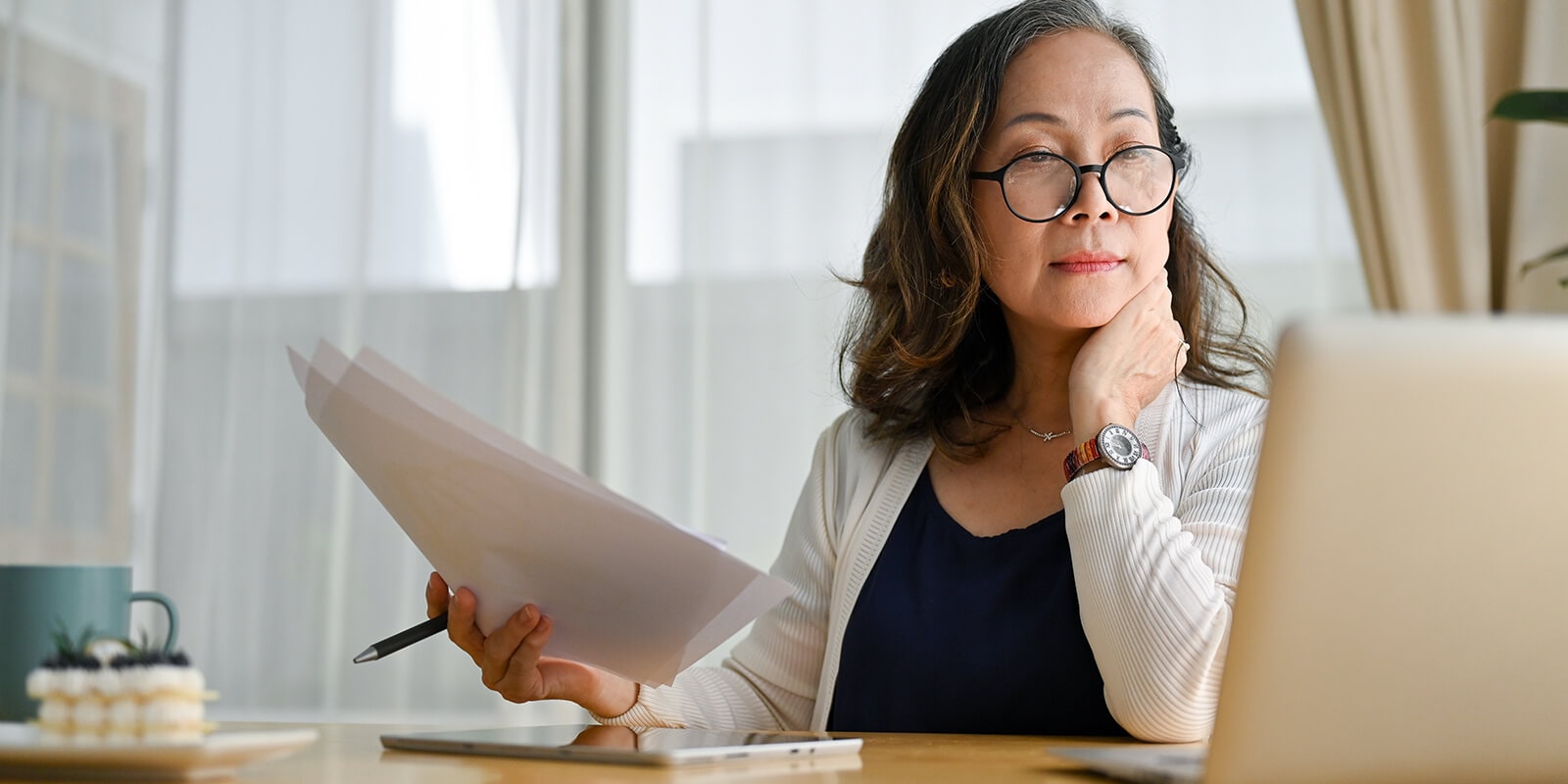 Teacher looks at laptop screen while holding papers in her hand