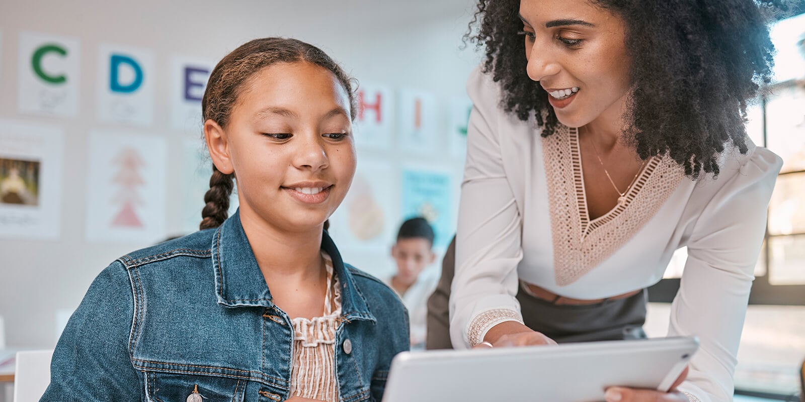Teacher helps student at her tablet while in a classroom