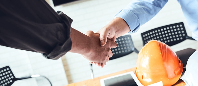 Two people shaking hands over building plans.