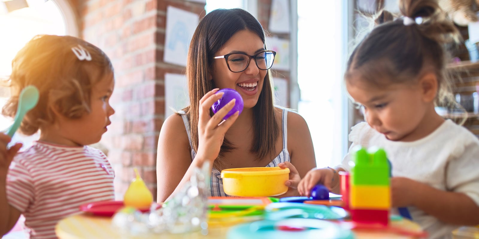 Teacher smiling while engaging two very young children with a set of blocks