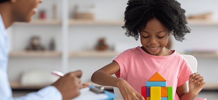 Child and threapist working together while the child plays with building blocks. 